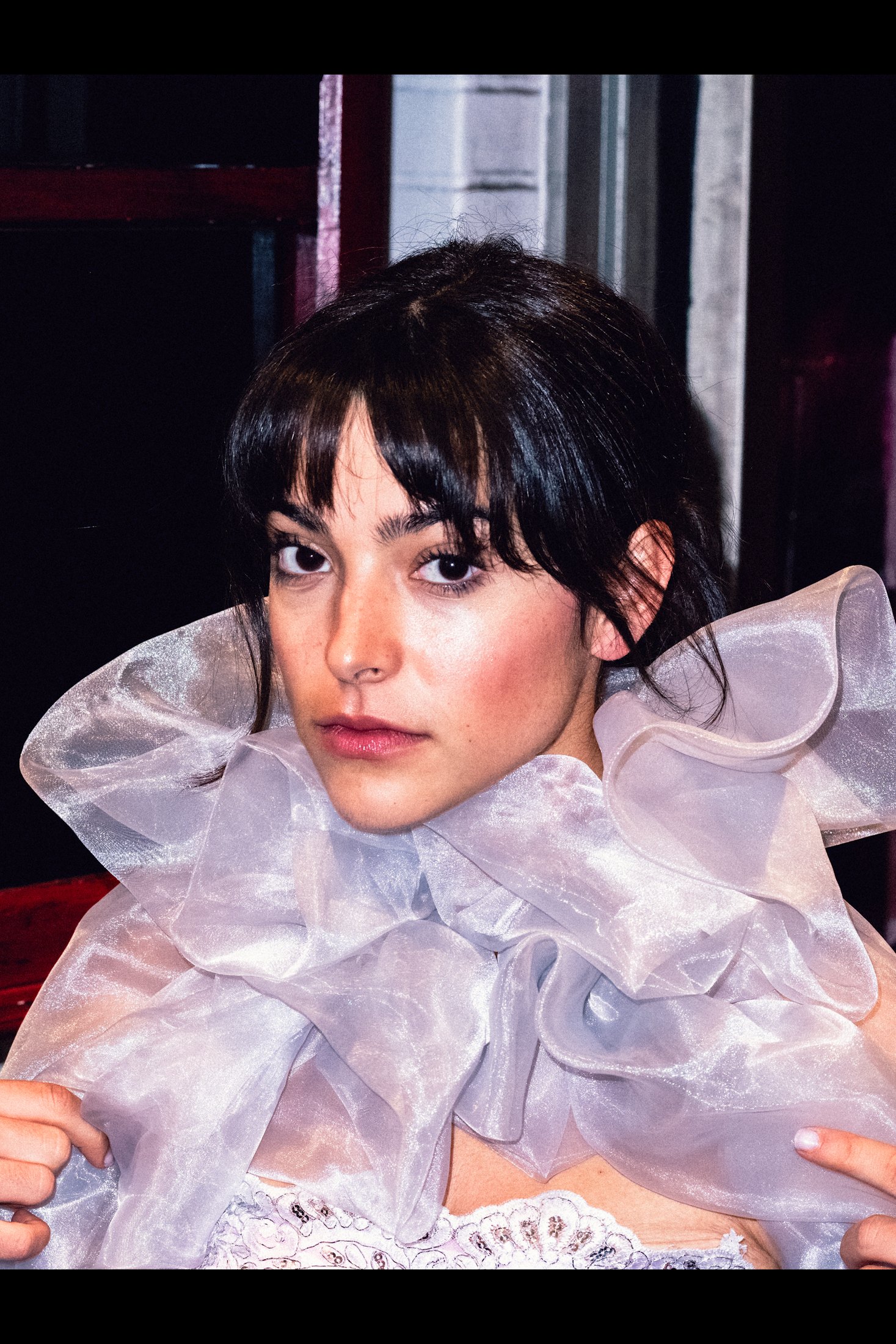 Model in a sheer sculptural ruff posing backstage after dark
